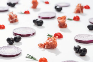 Kırmızı soğan halkaları ve beyaz arka plan üzerinde Siyah Zeytin yakınındaki çiğ jambon kiraz domates biberiye ile yakınındaki seçici odak çırpı