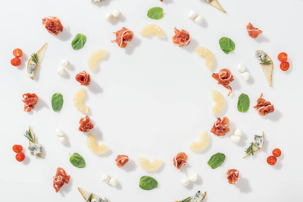 flat lay of prosciutto near sliced pineapples and healthy ingredients on white background