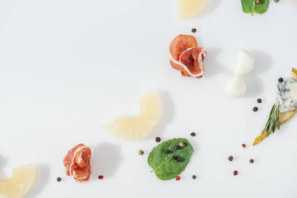 flat lay of sliced pineapples near tasty prosciutto and organic ingredients and spices on white background