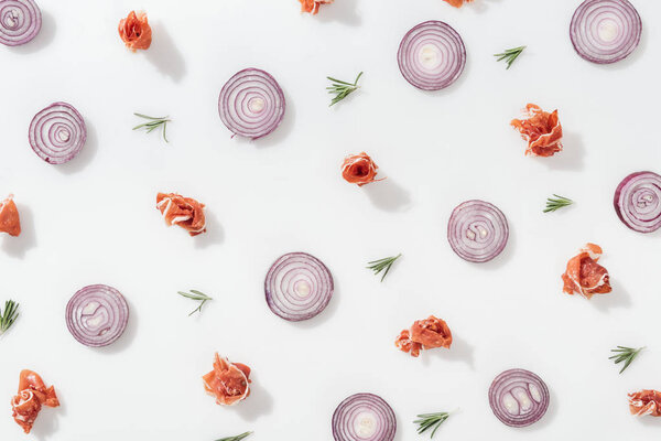 flat lay of red onion rings near tasty prosciutto and rosemary twigs on white background