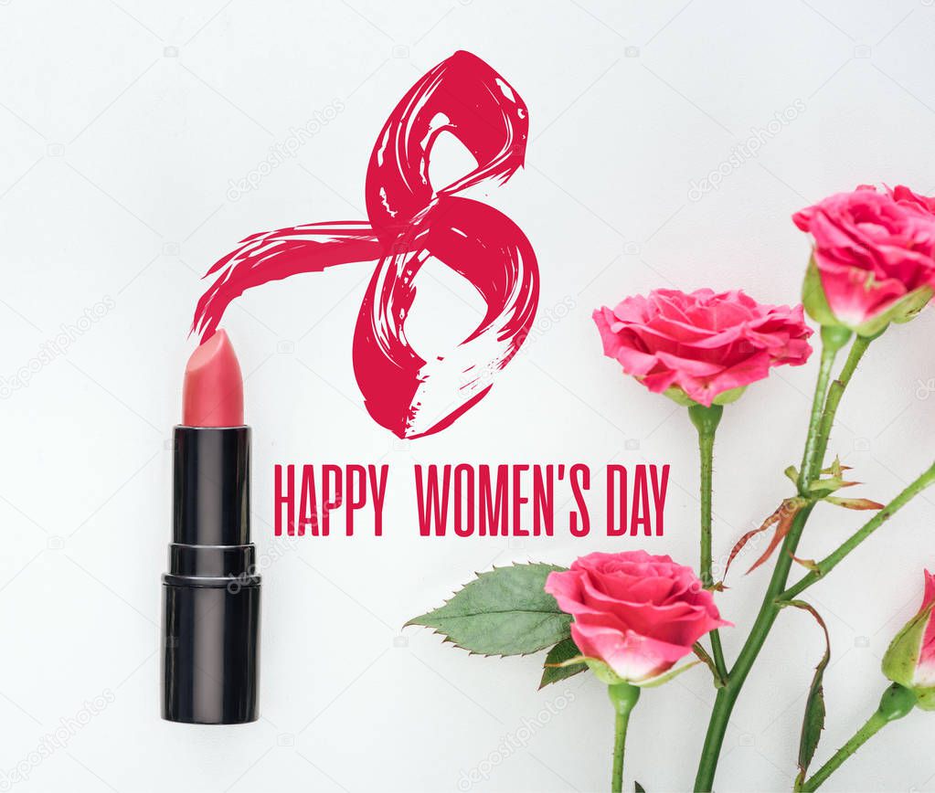 top view of lipstick and pink roses on white background with happy womens day lettering 