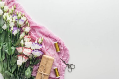 gri arka plan üzerinde eustoma, sarılmış hediye, iş parçacığının makaralar, makas ve pembe bir bez Üstten Görünüm