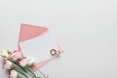 gri arka plan üzerinde pembe zarf, eustoma ve altın alyans ile boş kartı Üstten Görünüm