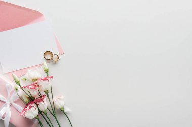 top view of empty card with pink envelope, flowers, wrapped gift and golden wedding rings on grey background clipart