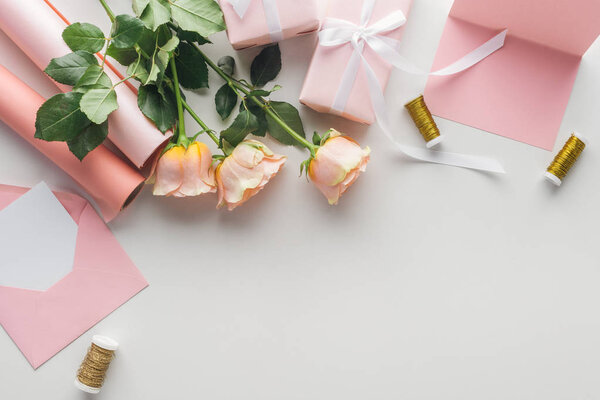 top view of pink roses, rolls of paper, wrapped gifts and envelope on grey background 