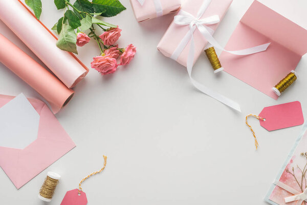 top view of pink roses, rolls of paper, wrapped gifts, envelope and greeting card on grey background 