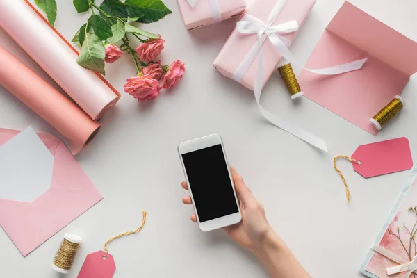 妇女拿着智能手机在玫瑰附近的裁剪视图 包裹的礼物 贺卡和线轴在灰色背景 — 图库照片