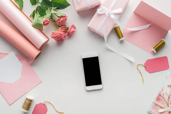 在灰色背景上的智能手机附近的最高视图玫瑰 包裹的礼物 信封和线轴线 — 图库照片
