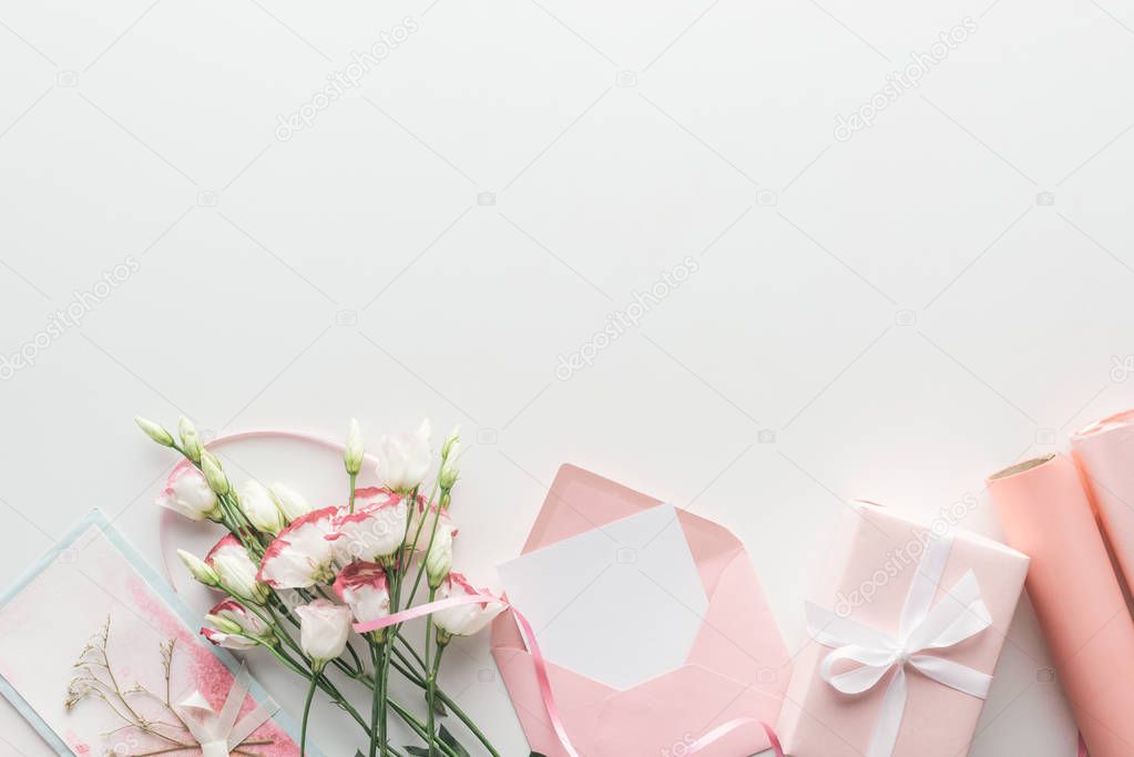 top view of pink eustoma, rolls of paper, wrapped gifts, envelope and greeting card on grey background  