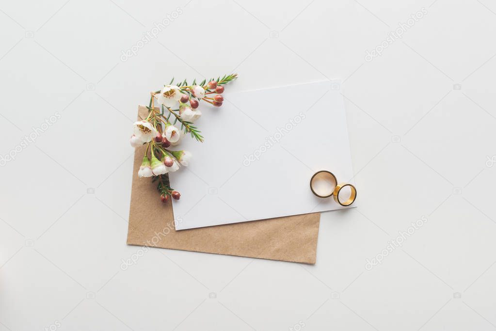 top view of empty card with brown craft paper envelope and wedding rings on grey background