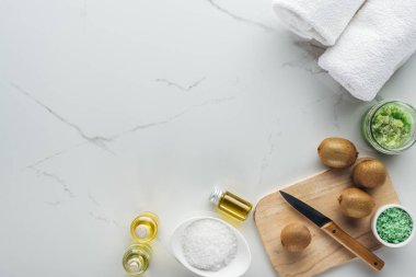 beyaz yüzey üzerinde kaseler ve kapsayıcılar kozmetik bileşenleri, havlu, bıçak ve kivi ile kesim masası ile Üstten Görünüm