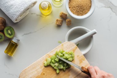 partial view of woman cutting kiwi on wooden cutting desk on white surface clipart