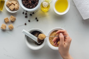 partial view of woman adding brown sugar into pounder with ground coffee on white surface clipart