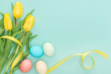 top view of yellow tulip flowers with ribbon and easter eggs isolated on blue with copy space clipart