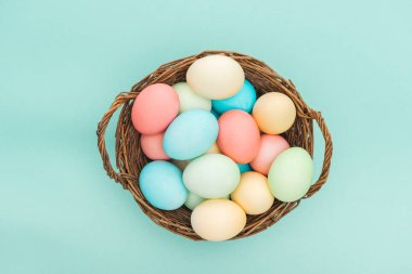top view of pastel easter eggs in wicker basket isolated on blue  clipart