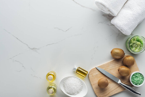 вид верхнего стола с вырезанным киви, а также различные натуральные компоненты для домашней косметики на белой поверхности
