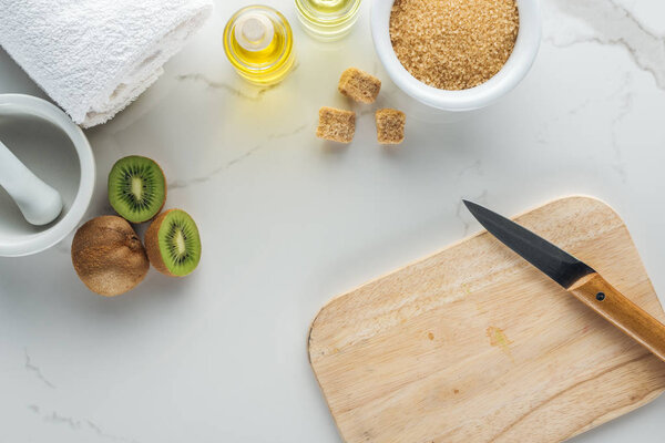 top view of various natural ingredients for cosmetics making, and cutting desk with kiwi on white surface