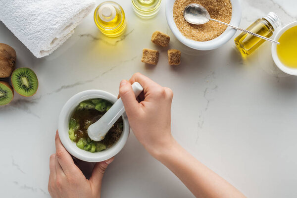 cropped view of woman smashing kiwi in pounder on white surface