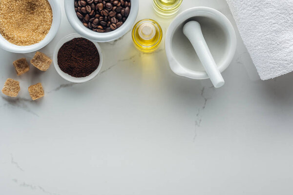 top view of pounder and different natural ingredients in bowls and bottles on white surface