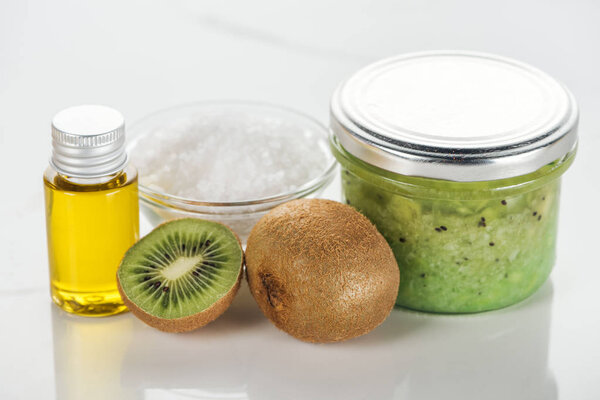 selective focus of glass containers with kiwi puree and oil, bowl of salt, and kiwi on white surface
