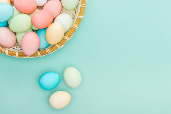top view of traditional pastel easter eggs in wicker plate isolated on blue with copy space