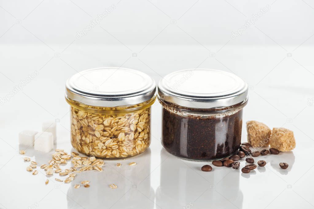 glass jars with homemade scrub and cosmetic mask on white surface