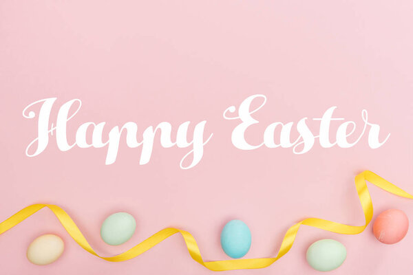 Happy Easter lettering with painted eggs and ribbon isolated on pink