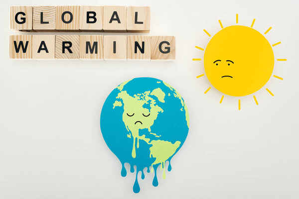 paper cut melting earth and sun with sad face expressions, thermometer with high temperature on scale, and "global warming" lettering on wooden cubes on grey background