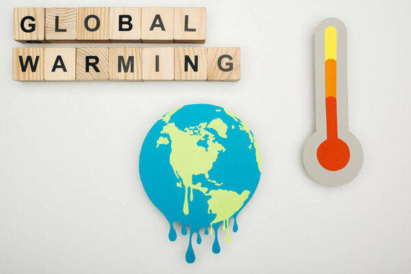 paper cut melting earth, wooden cubes with "global warming" lettering, and thermometer with hign temperature indication on scale on grey background