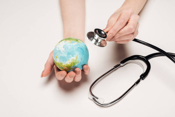 cropped view of woman holding stethoscope and globe model on white background, global warming concept