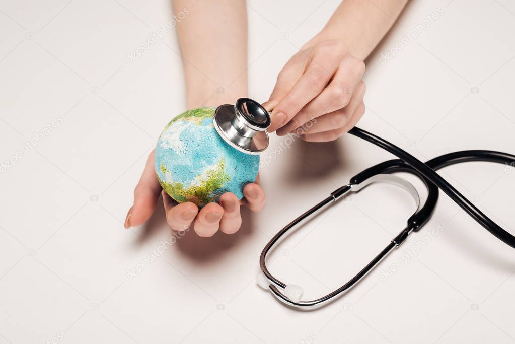 partial view of woman holding stethoscope and earth model on white background, global warming concept