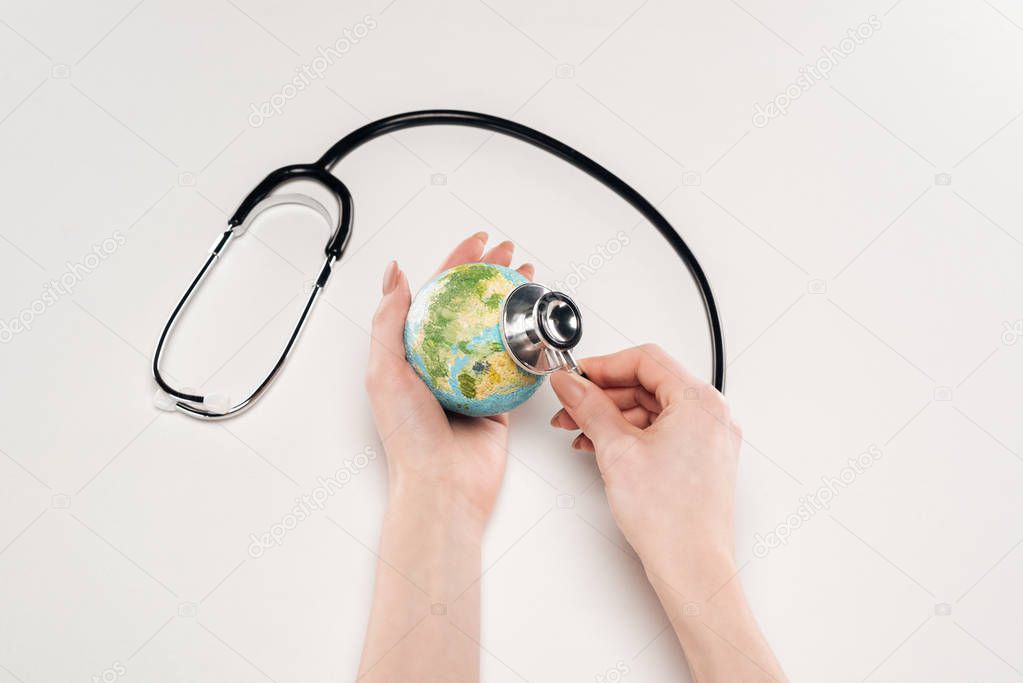 partial view of woman holding stethoscope and earth model on white background, global warming concept