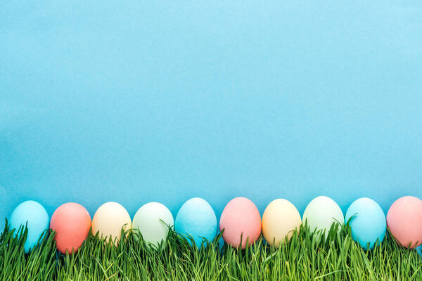 top view of colorful easter eggs on grass isolated on blue