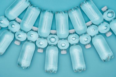 şeffaf plastik su şişeleri üzerinde turkuaz izole satırlar halinde yerleştirilmiş, üstten görünüm