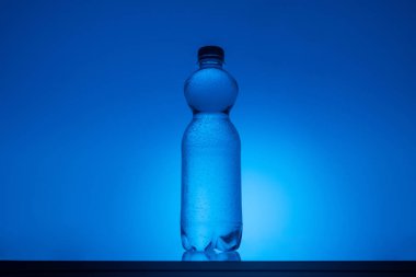 arkadan aydınlatmalı neon mavi zemin üzerine şeffaf plastik su şişesi tonlu görüntü