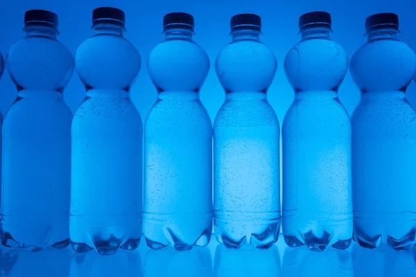 Imagen Tonificada Botellas Agua Plástico Fila Sobre Fondo Azul Neón —  Fotos de Stock