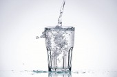 water pouring in glass on white background with backlit, splashes and copy space