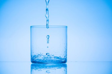 toned image of water pouring in empty glass on blue background clipart