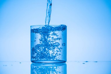 toned image of water pouring in full glass on blue background clipart