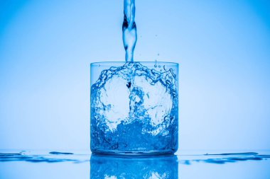 toned image of water pouring in drinking glass on blue background with splashes clipart