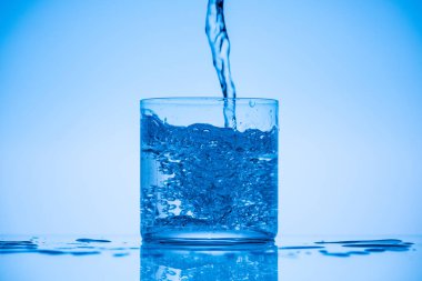 toned image of water pouring in glass on blue background with splashes and copy space clipart