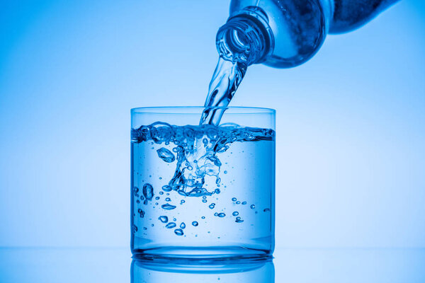 water pouring from plastic bottle in glass on blue background