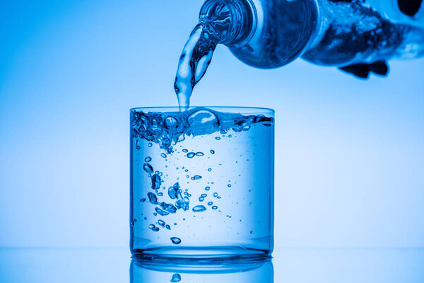 partial view of man pouring water from plastic bottle in glass on blue background