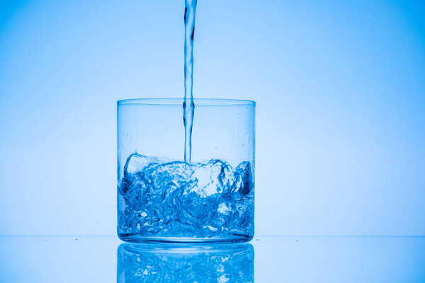 toned image of water pouring in glass on blue background with copy space