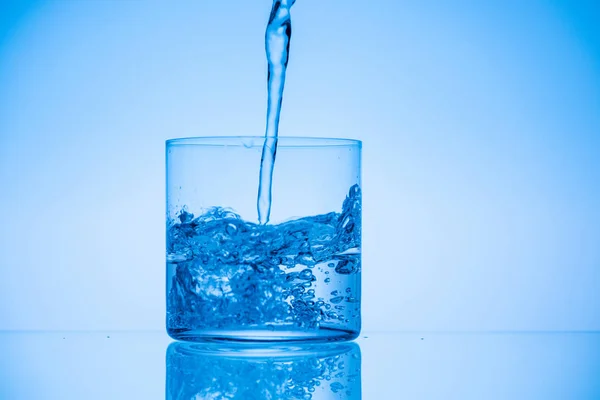 Imagem Tonificada Água Derramando Vidro Fundo Azul Com Espaço Cópia — Fotografia de Stock