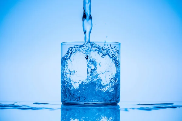 Imagem Tonificada Água Derramando Vidro Beber Fundo Azul Com Salpicos — Fotografia de Stock