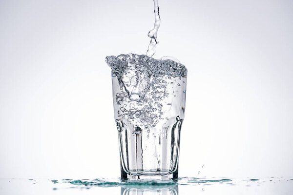 water pouring in glass on white background with backlit, splashes and copy space