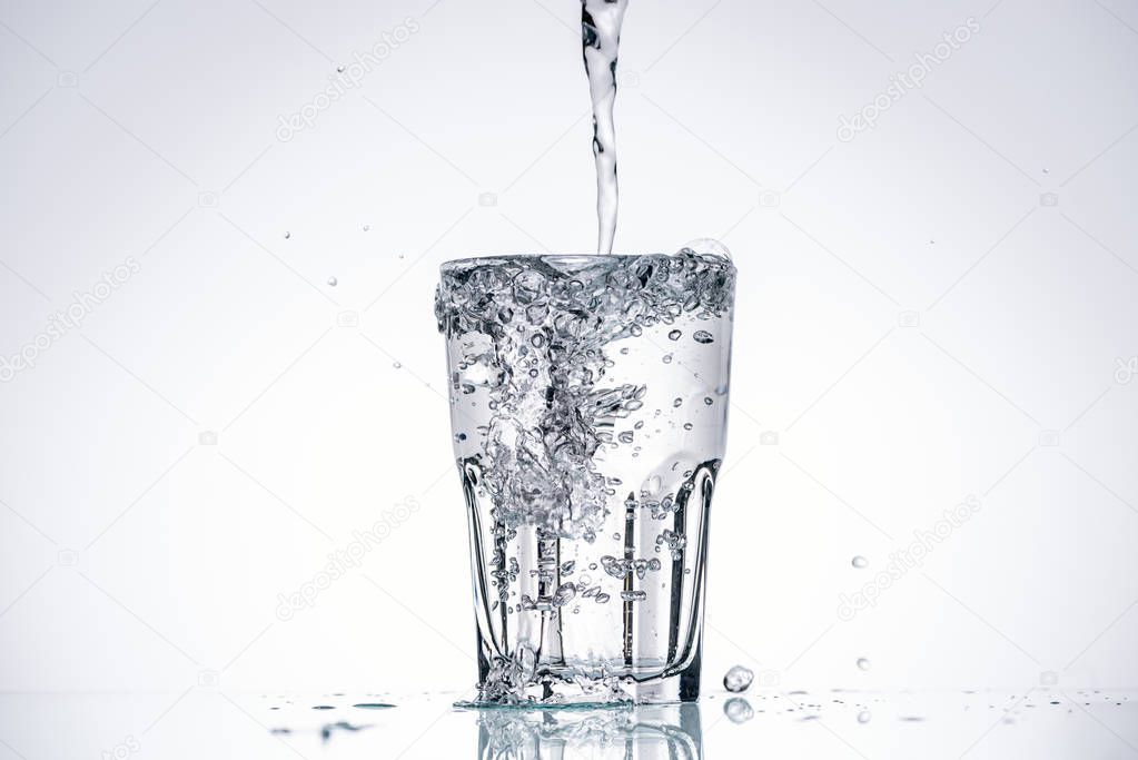 water pouring in full glass on white background with backlit and splashes