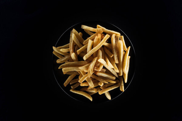 top view of tasty french fries on plate isolated on black