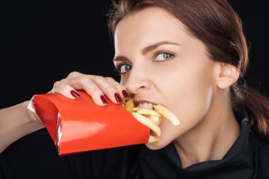 çekici kadın siyah izole kamera bakarken tuzlu patates kızartması yemek